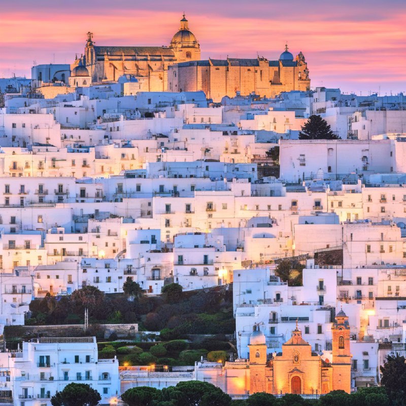 #Bing_Wallpaper“梦幻般的日落映照在意大利普利亚大区的奥斯图尼，这座被称为‘白色之城’的迷人山城，古老的白色建筑在暮色降临时沐浴在温暖的琥珀色和金色光辉中
