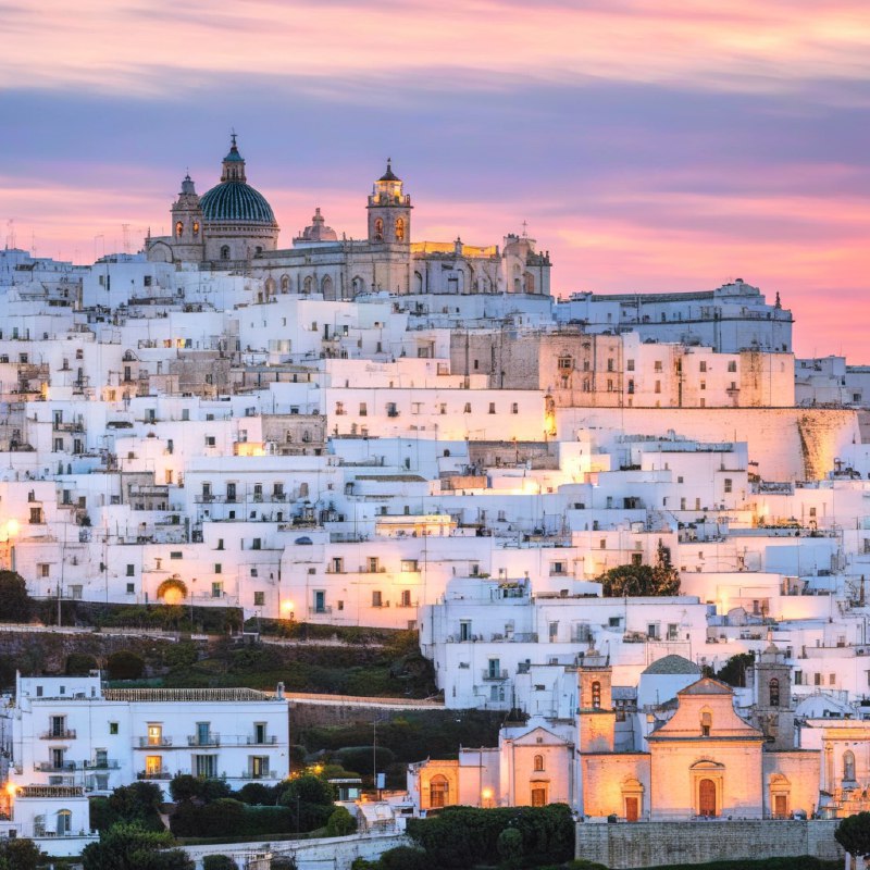 #Bing_Wallpaper“梦幻般的日落映照在意大利普利亚大区的奥斯图尼，这座被称为‘白色之城’的迷人山城，古老的白色建筑在暮色降临时沐浴在温暖的琥珀色和金色光辉中