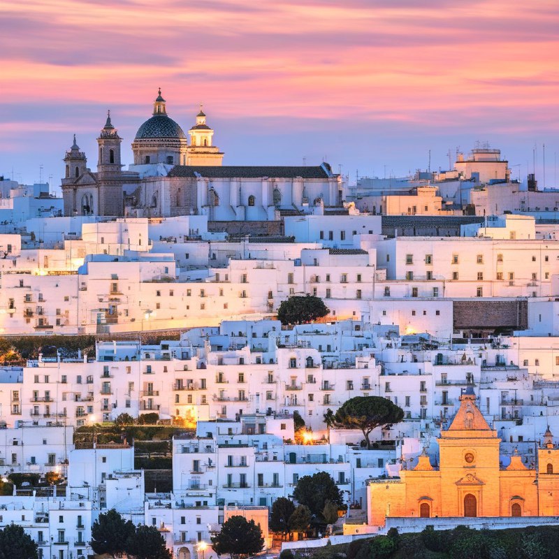 #Bing_Wallpaper“梦幻般的日落映照在意大利普利亚大区的奥斯图尼，这座被称为‘白色之城’的迷人山城，古老的白色建筑在暮色降临时沐浴在温暖的琥珀色和金色光辉中