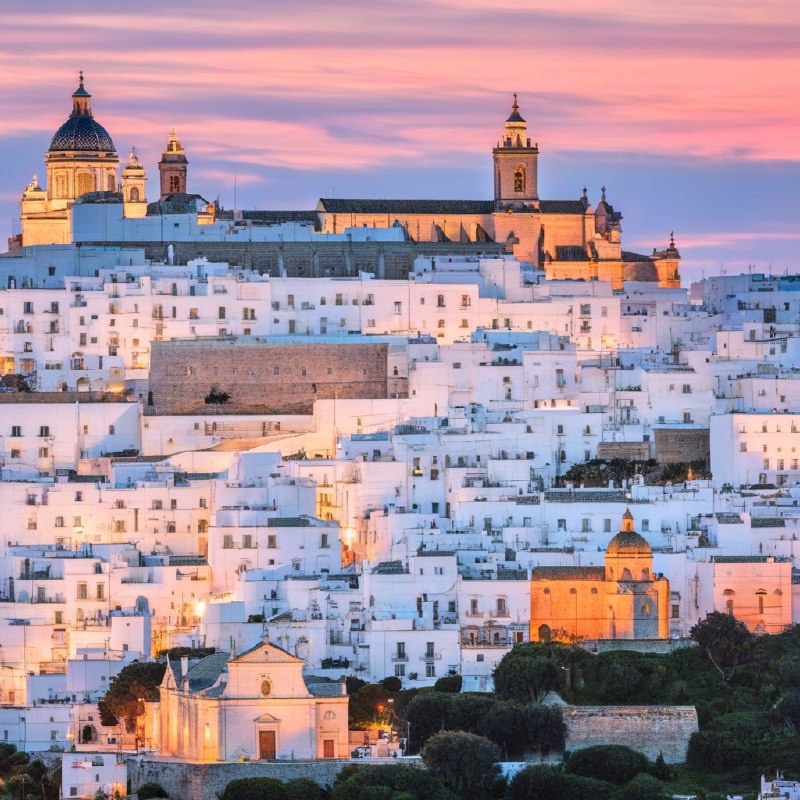 #Bing_Wallpaper“梦幻般的日落映照在意大利普利亚大区的奥斯图尼，这座被称为‘白色之城’的迷人山城，古老的白色建筑在暮色降临时沐浴在温暖的琥珀色和金色光辉中