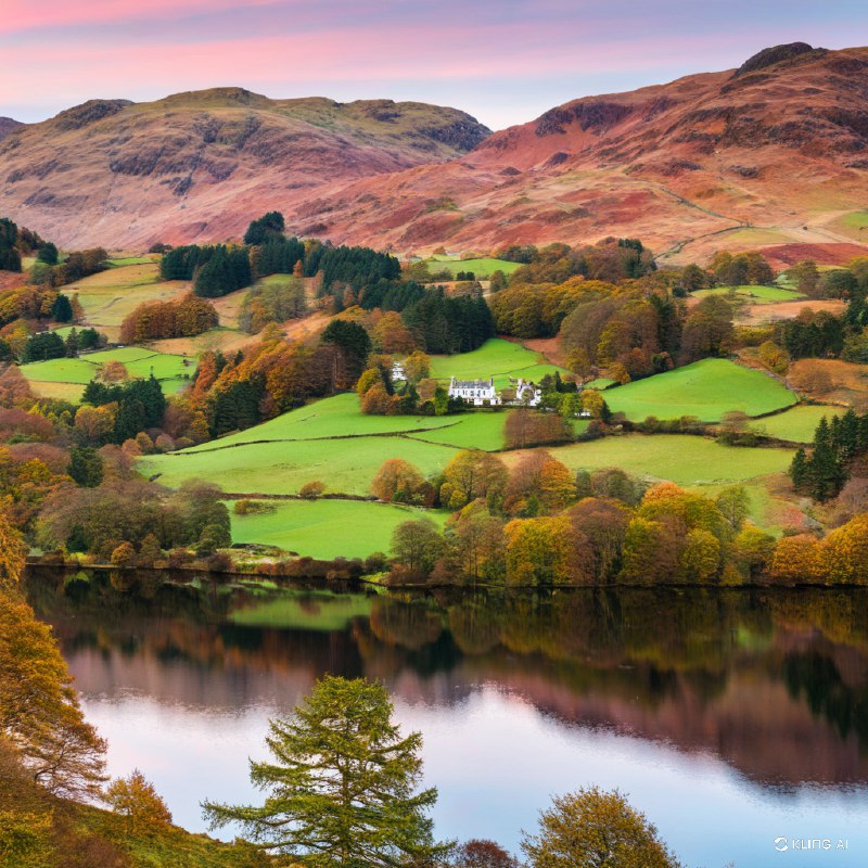 秋季的英格兰湖区格拉斯米尔风景宁静如画，平静的湖面倒映着秋叶的缤纷色彩，翠绿的草地和连绵起伏的山丘在粉色的天空下交相辉映